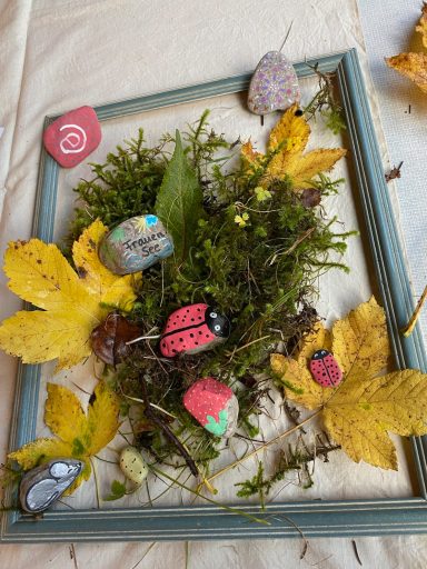 Rahmen mit Moos, bunten Steinen und herbstlichen Blättern dekoriert.