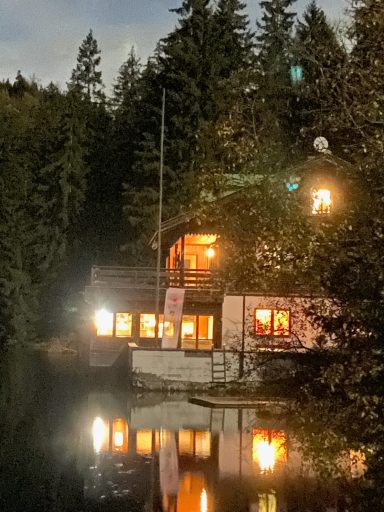 Hübsches Holzhaus am See, umgeben von Bäumen, mit warmem Licht bei Nacht.