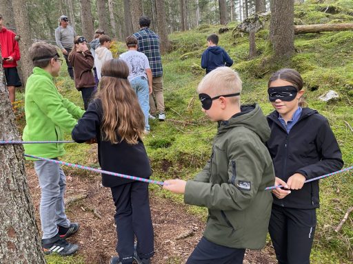 Kinder mit Schlafmasken üben Teamarbeit im Wald, indem sie an einem Seil ziehen.