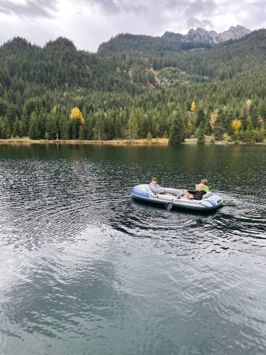 Eine Person paddelt in einem Schlauchboot auf einem ruhigen See, umgeben von Wäldern.